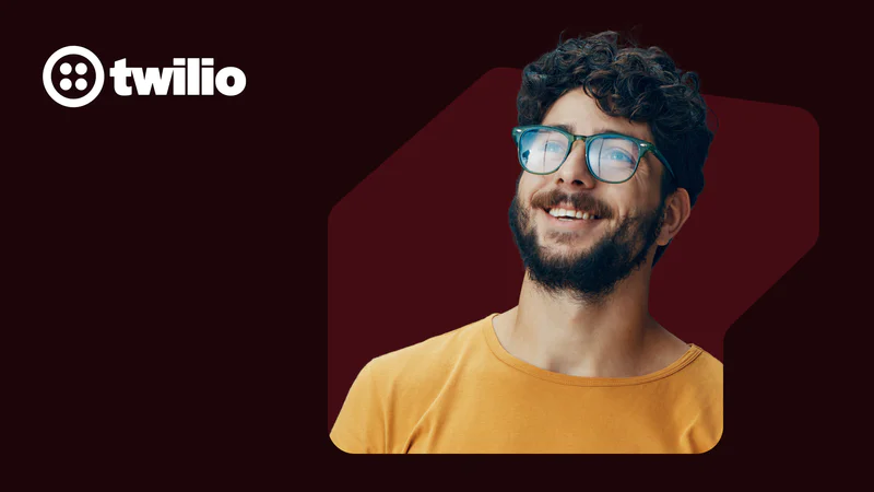 Smiling man wearing glasses and a yellow shirt with Twilio logo on a dark red background.