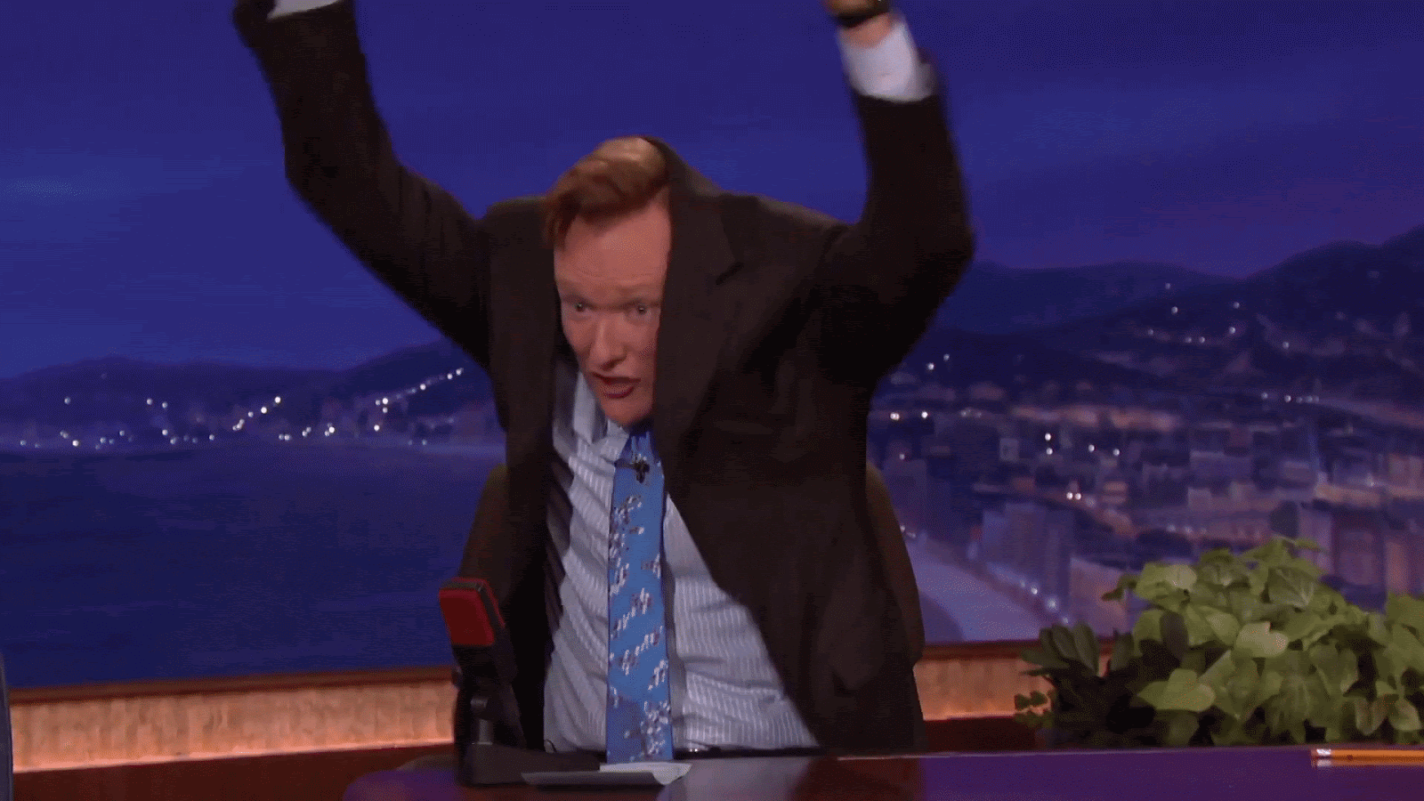 gif of Conan O&#39;Brien in a tie and button up shirt, with his blazer pulled up over his head, waving his arms and making a goofy face.