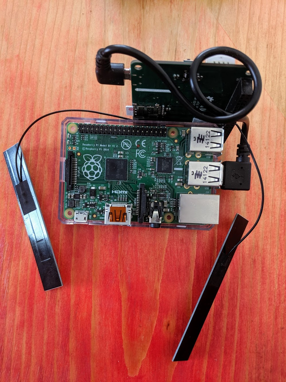 A Raspberry Pi sits on a table. A LTE Cat 1 Pi HAT is attached via the USB-A to micro USD ports. The hat sits next to the pi, but not on top of it, and the HAT has antennas attached.