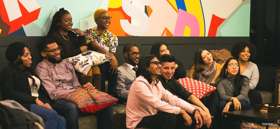 Diverse group of friends smiling and sitting close together on a sofa indoors.