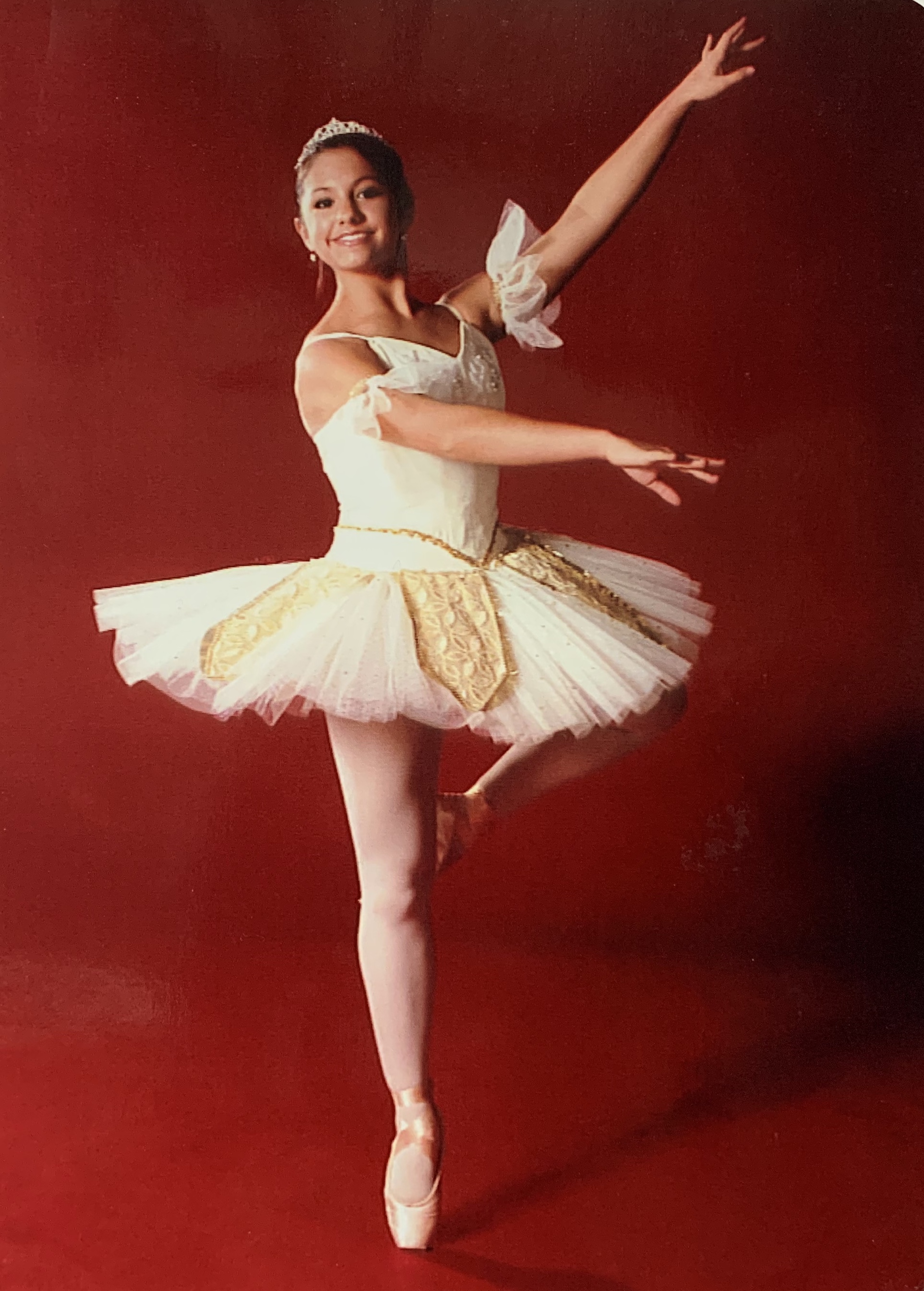 Photo of Liz Moy in a ballet position wearing a tutu against a red background