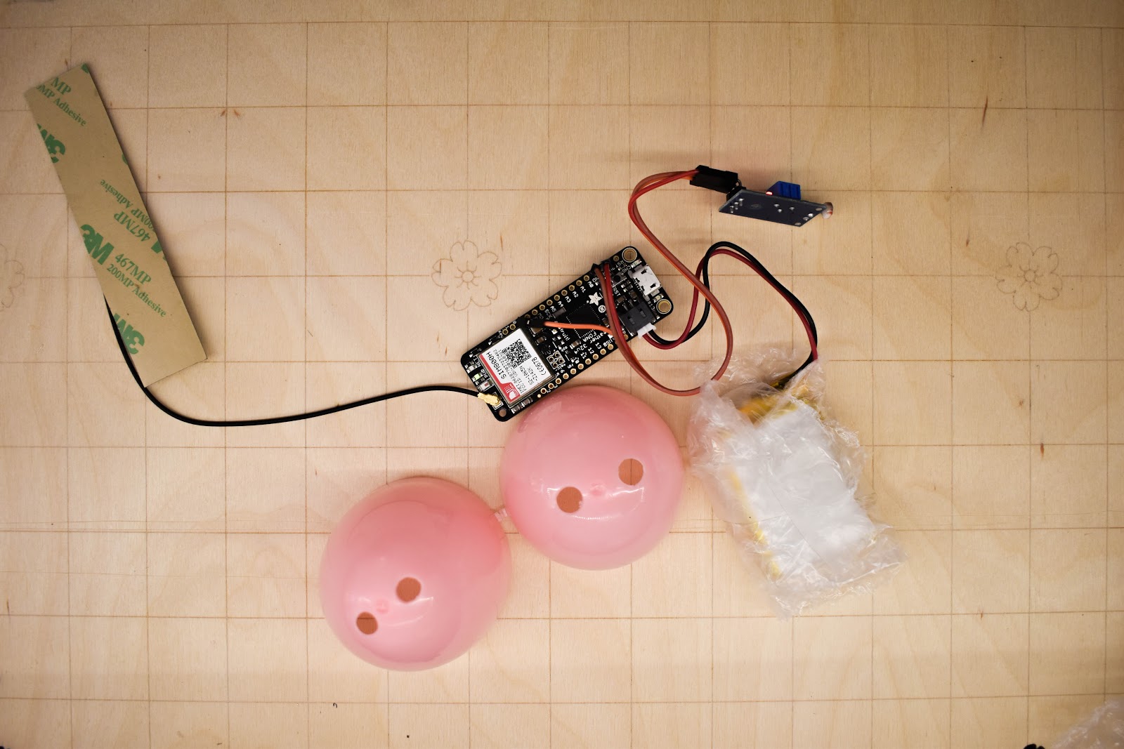 The Adafruit FONA with attached light sensor and battery. The battery is wrapped in bubble wrap. There is also an easter egg with four holes drilled in it.