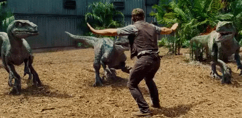 animated gif of a man surrounded by velociraptors, holding his arms out and backing away slowly.
