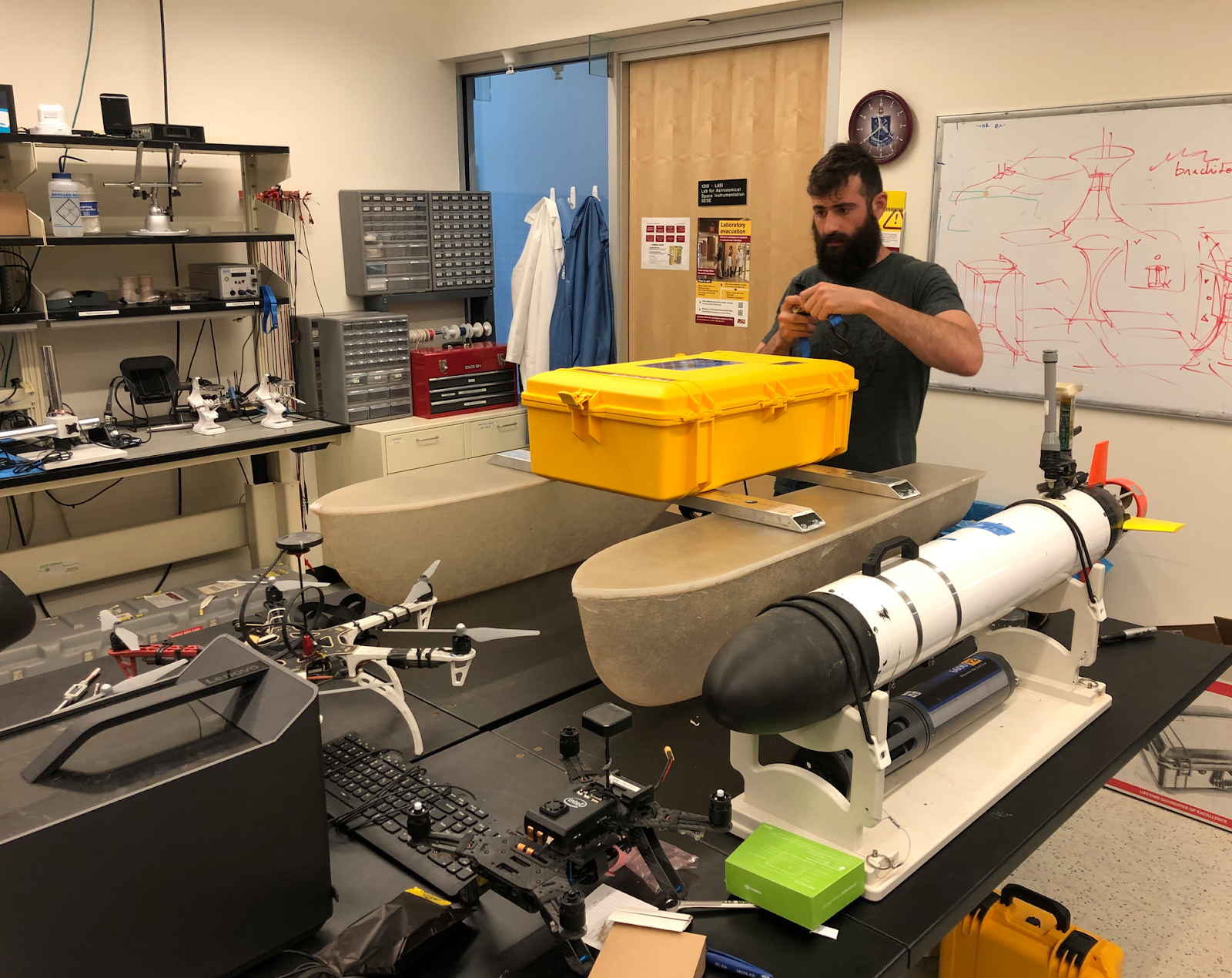 Alex working on a robotic boat he built in a lab surrounded by drones and an underwater robot