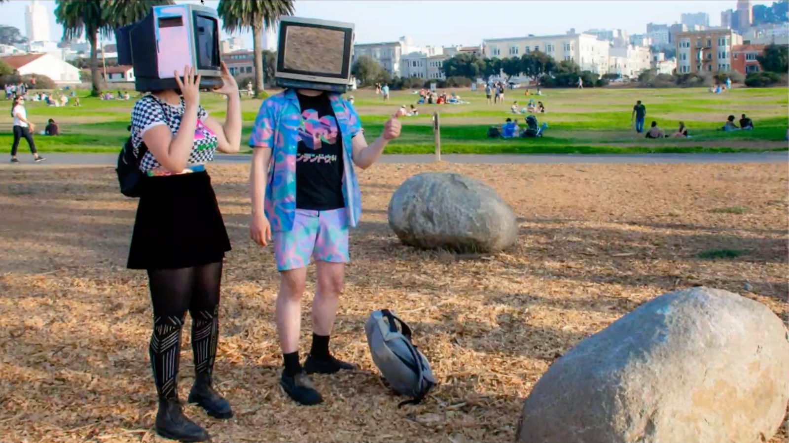 Two vaporloop participants, one in a black skirt and tights with a CRT on their head and one with a bright blue button down shirt and shorts with a CRT on their head.