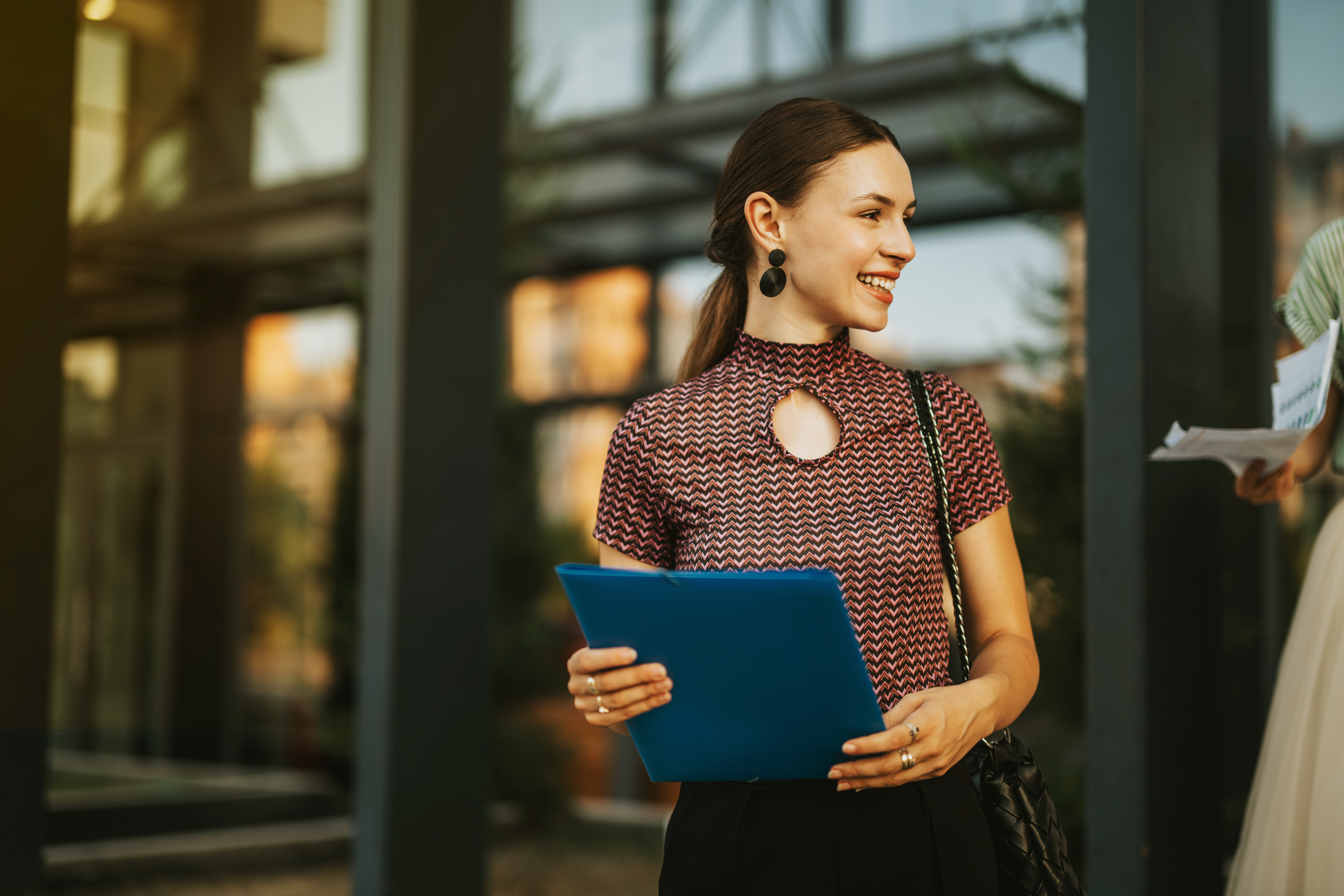 Smiling woman holding a blue folder standing outside a modern office building