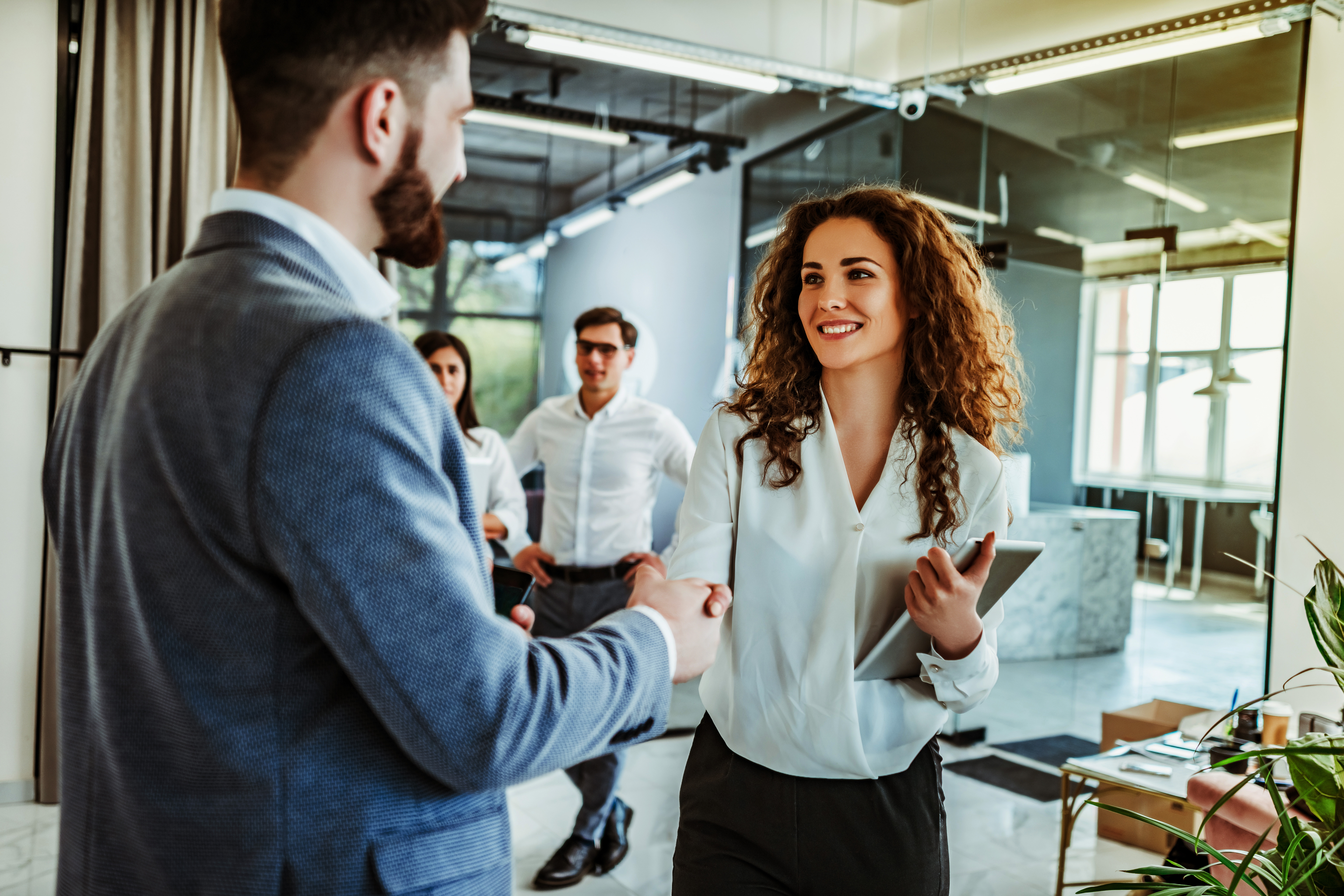 Business people shaking hands in an office while colleagues watch in the background.