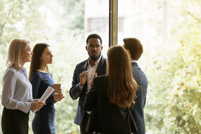 Group of professionals having a discussion in front of a large window with greenery outside.