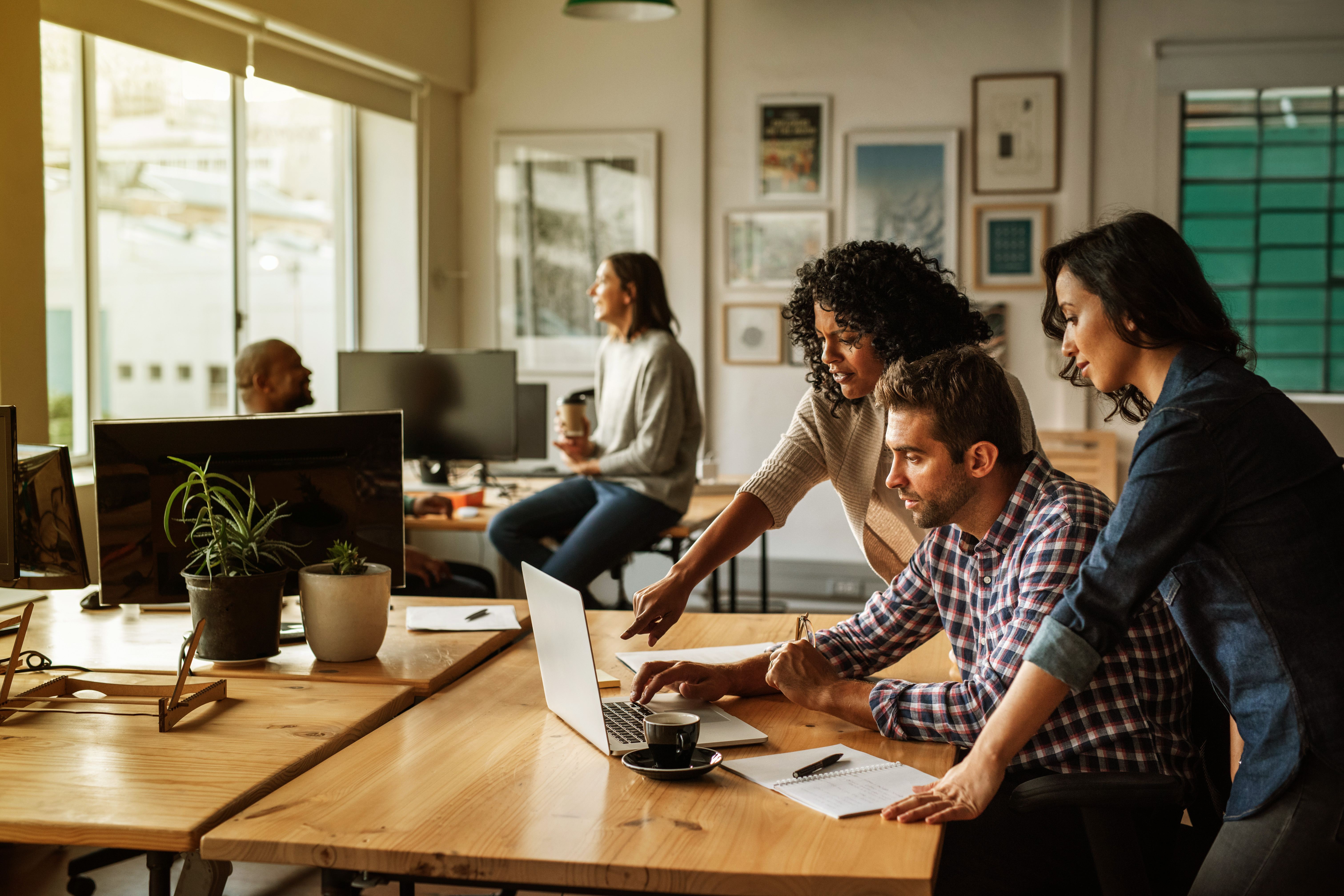 Team members collaborating on a laptop in a modern office with two people in the background.