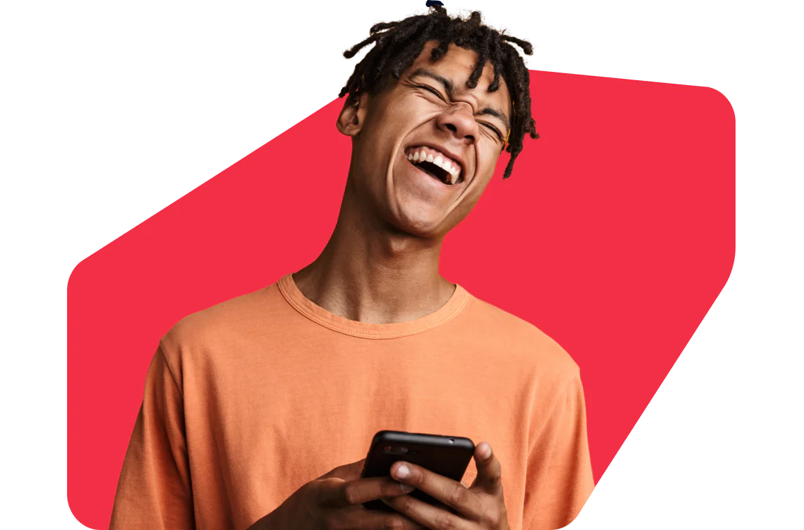 Smiling young man in an orange shirt holding a smartphone against a red geometric background.