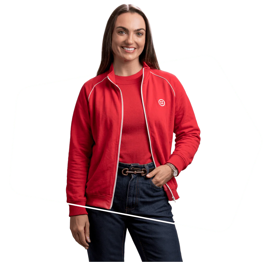 Woman wearing a red jacket over a red shirt, smiling with hands in jeans pockets.