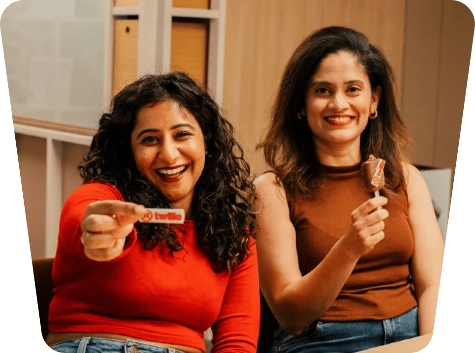 Two women sit together, one holding a Twilio item and the other enjoying an ice cream bar.
