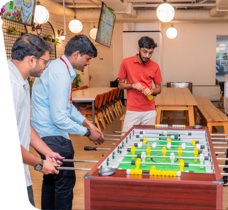 Three office workers playing foosball, with one person watching and holding a drink