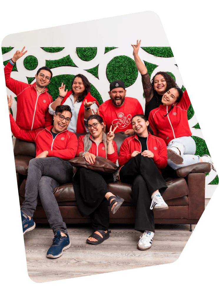 Group of seven people in red jackets posing excitedly on a couch in front of a green and white backdrop.