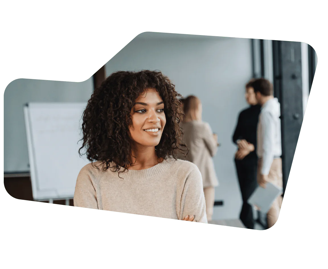 Woman smiling in the foreground with colleagues talking in the background by a whiteboard.