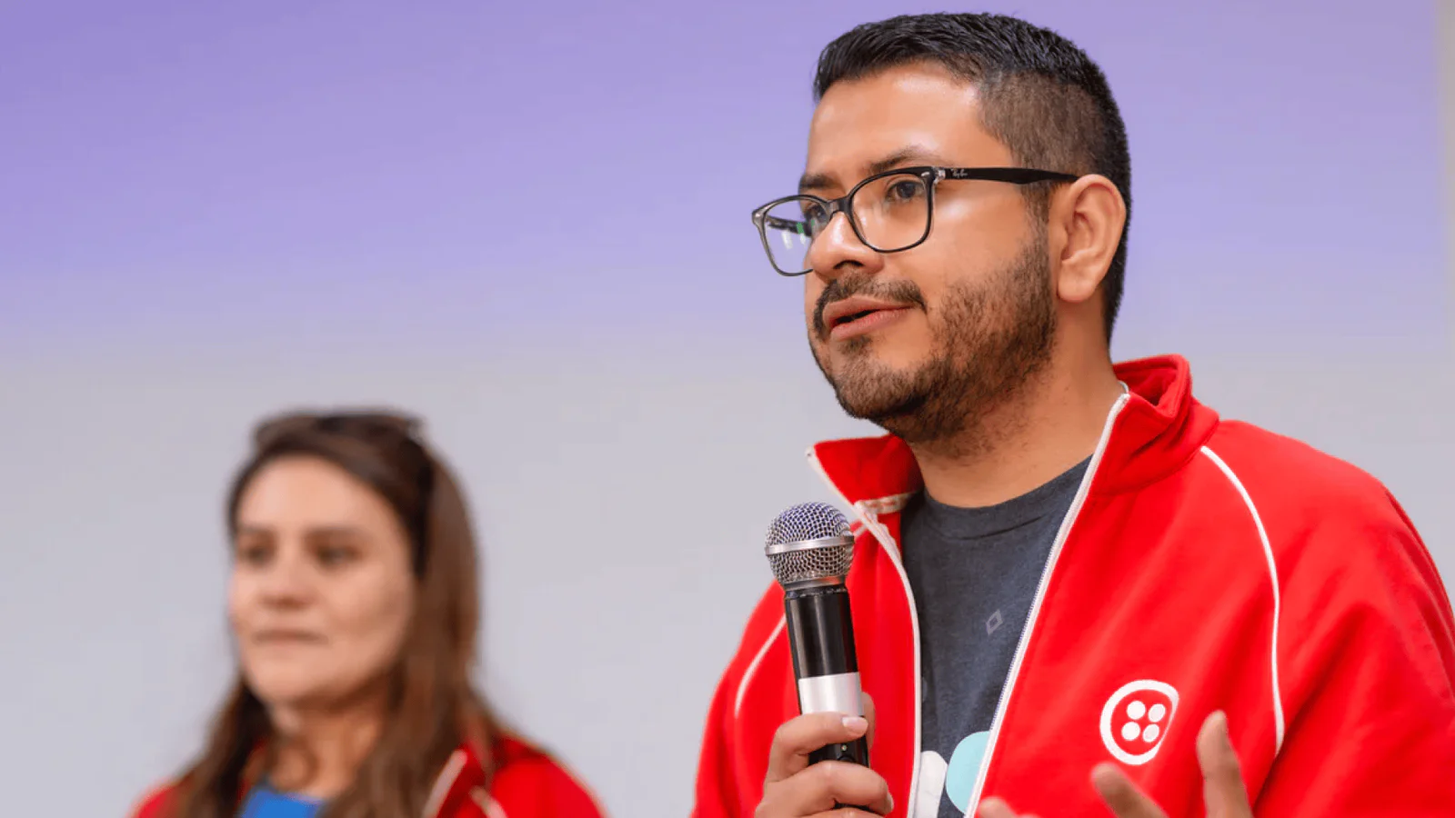 Two people wearing red jackets, one speaking into a microphone.