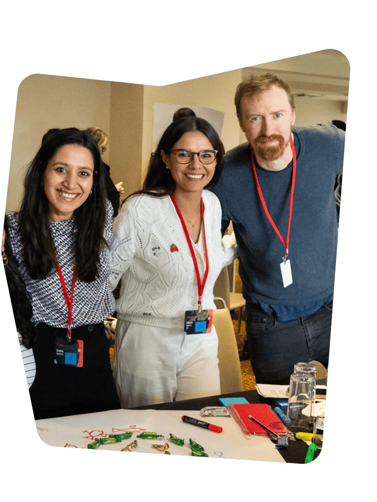 Three people at a table with workshop materials, smiling and wearing red lanyards.