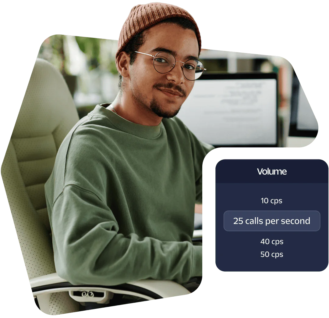 A person wearing glasses and a beanie sitting at a desk with a computer screen showing call volume data.