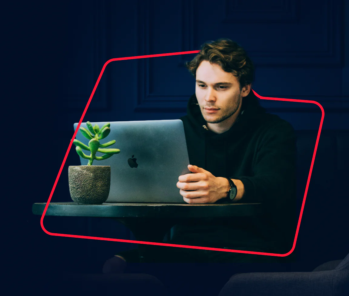 Man focused on a laptop with a small plant beside him on the table, surrounded by a red rectangular frame.