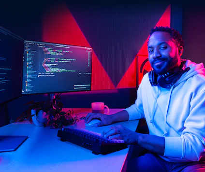 Software Developer Coding at Dual Monitors A man wearing headphones working on a dual-monitor computer setup with code displayed on the screens.