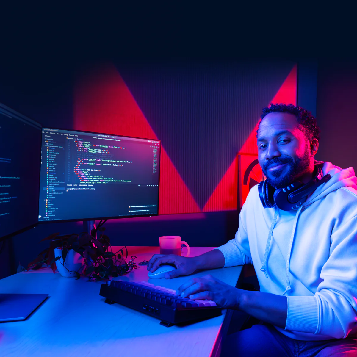 Software Developer Coding at Dual Monitors A man wearing headphones working on a dual-monitor computer setup with code displayed on the screens.