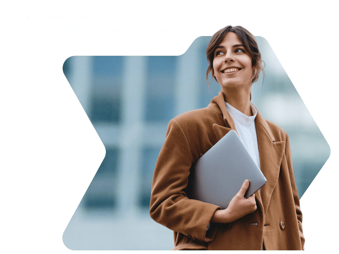 Woman in brown coat smiling and holding a laptop with a birthday discount notification from OWLCLOTHES