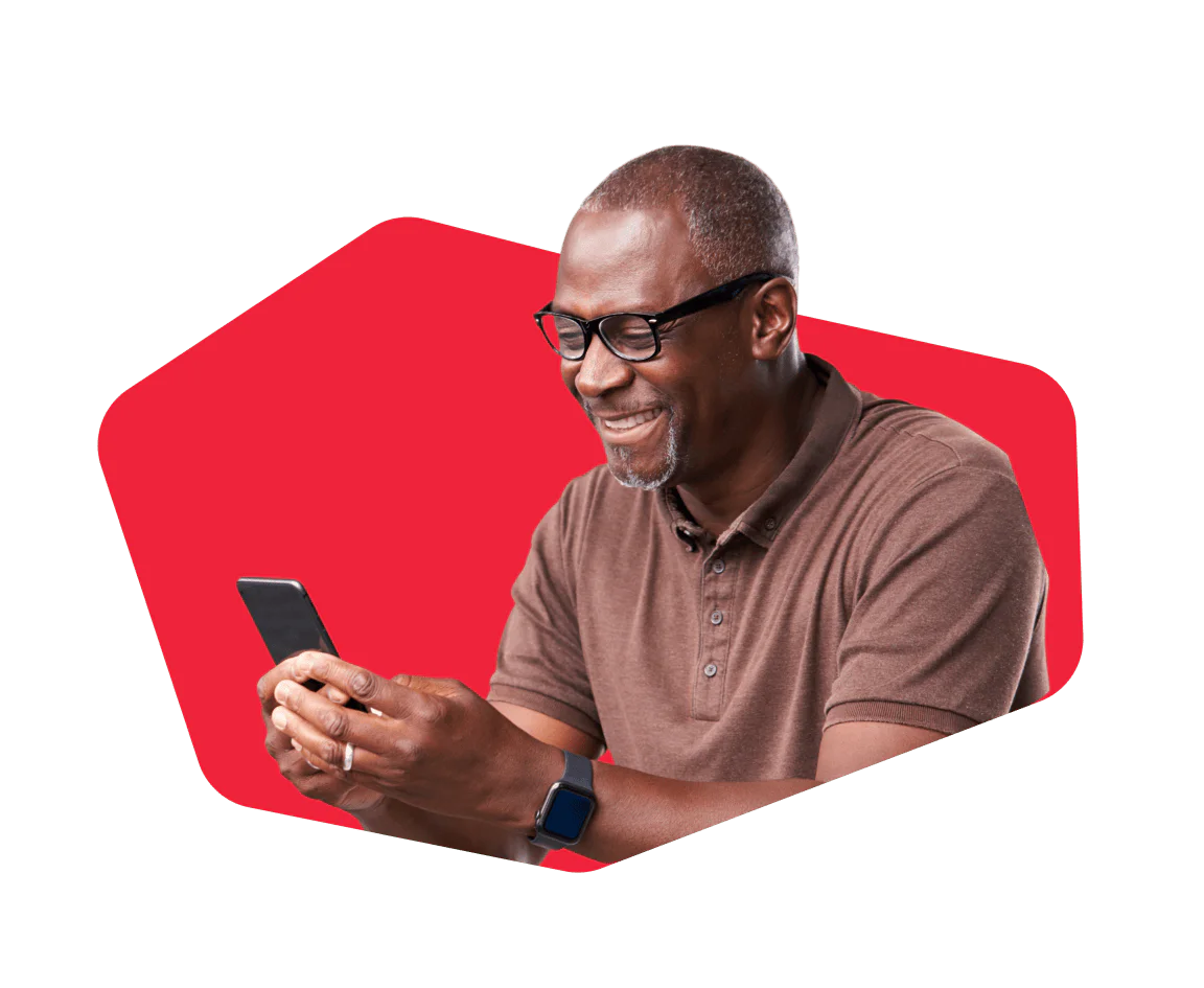 Smiling man with glasses using a smartphone against a red background.