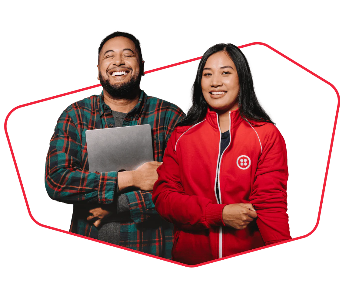 Two diverse people, one holding a laptop and the other in a red jacket, smiling confidently