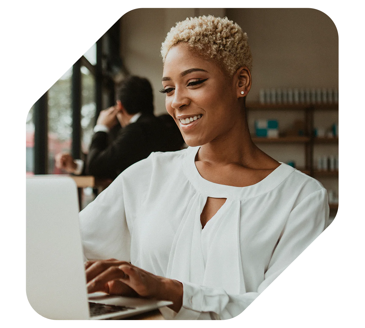 Woman in white blouse smiling and using a laptop inside a cafe.