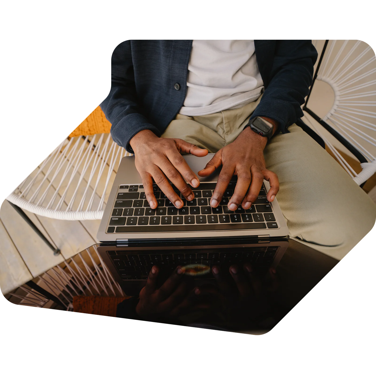 Hands typing on a laptop keyboard while seated with a smartwatch visible on the wrist.