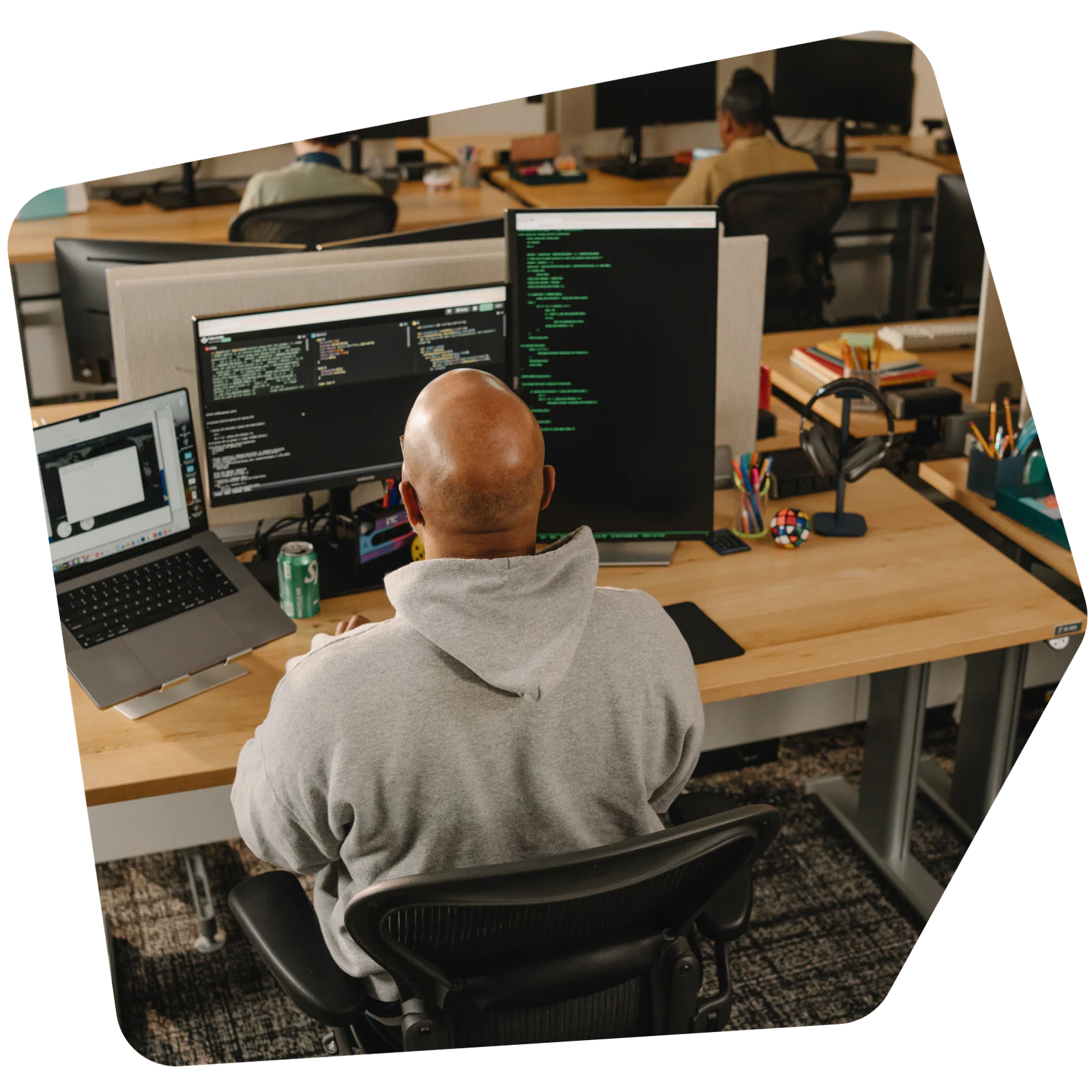 A person in a gray hoodie programming on dual monitors in an office environment.