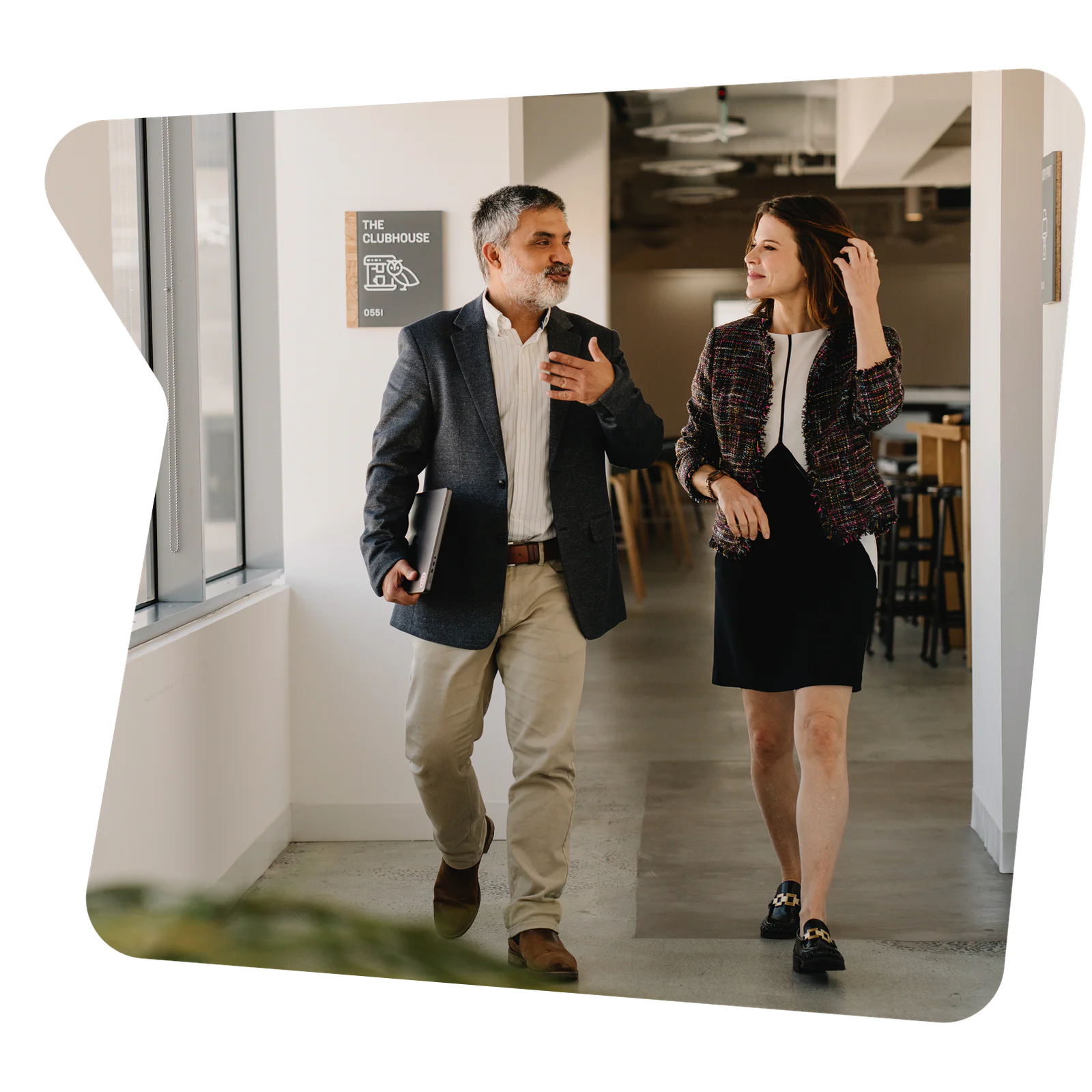Two colleagues walking and conversing in a modern office hallway.