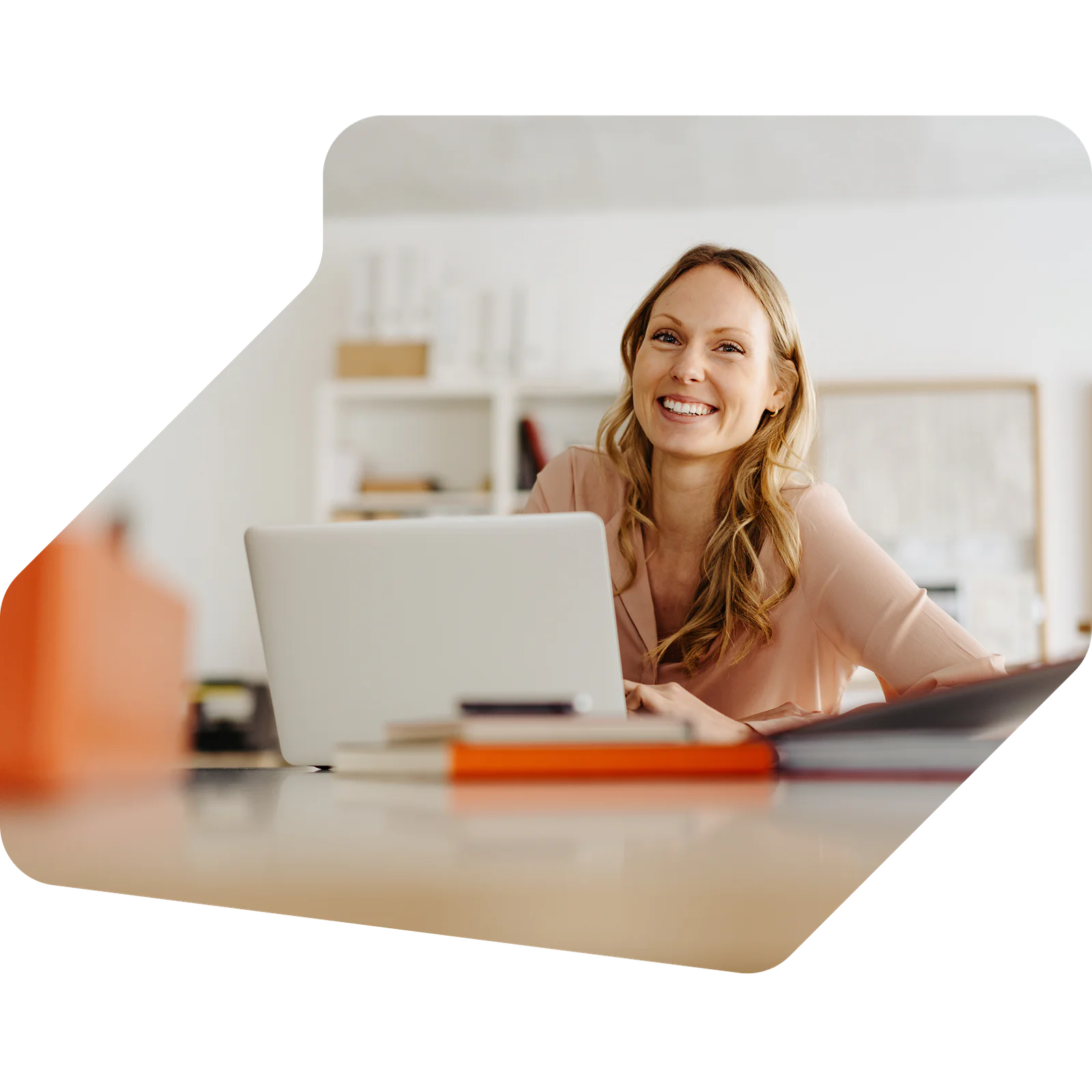 Woman smiling and working on a laptop with books on a desk