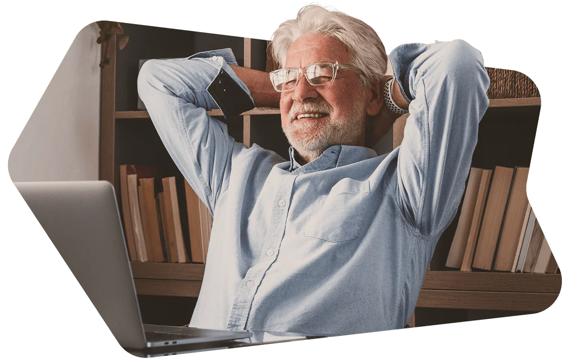 Senior man with gray hair, wearing glasses, sitting back comfortably and smiling at a laptop.