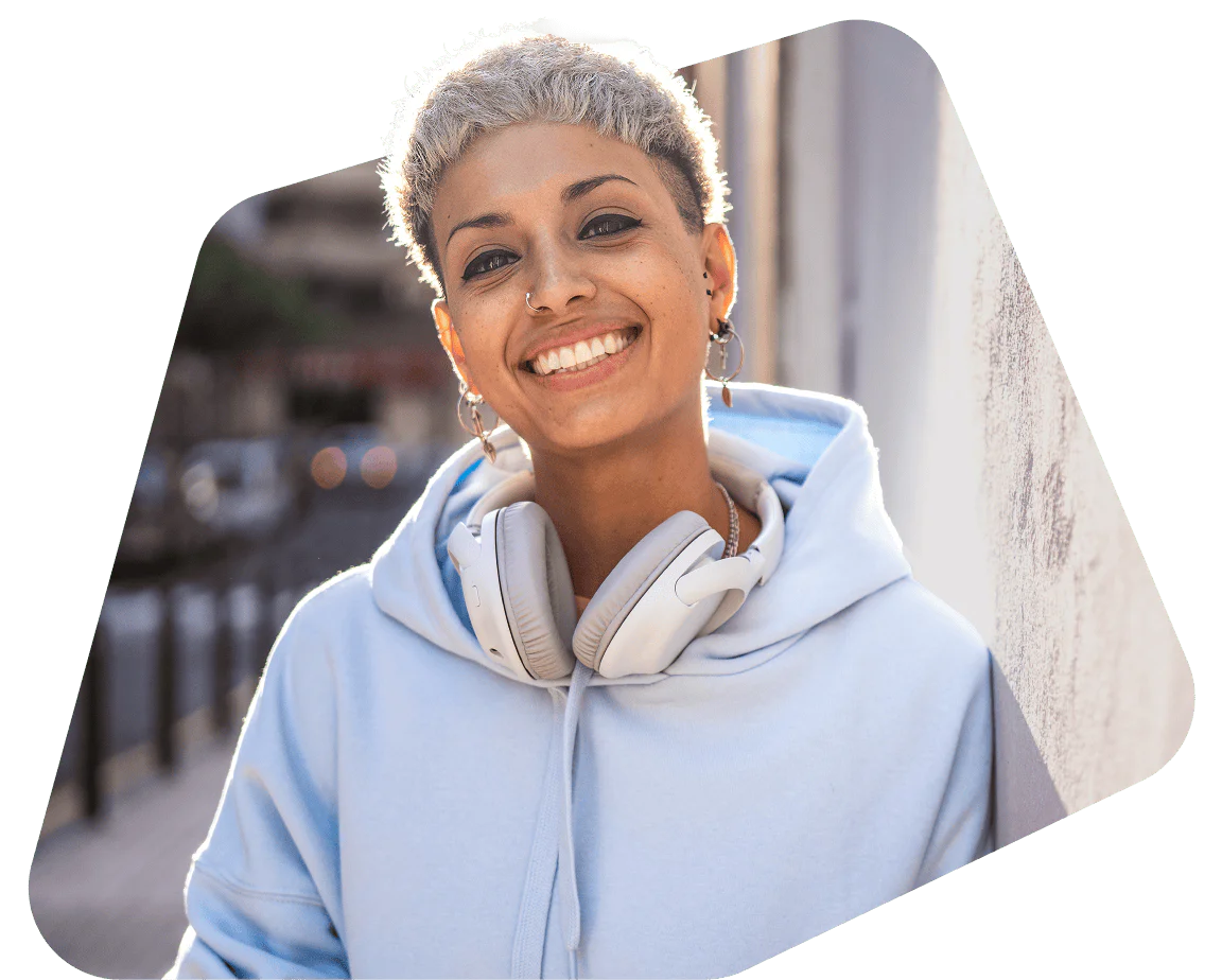 Person with short hair smiling and wearing headphones around their neck and a hoodie.