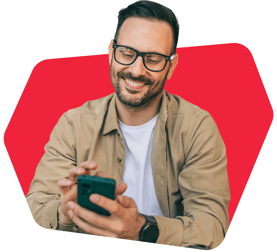 Man with glasses smiling while using smartphone, with red background.