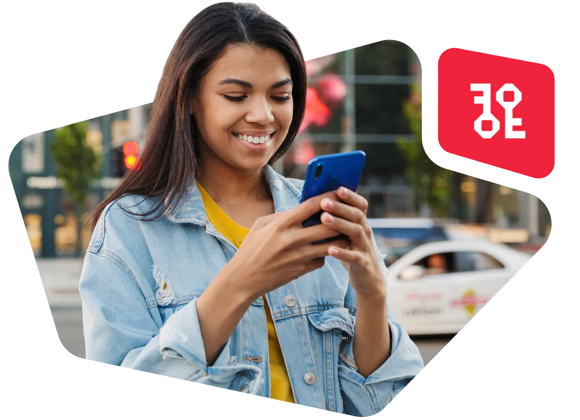 Young woman in a denim jacket smiling and looking at her smartphone on a city street.