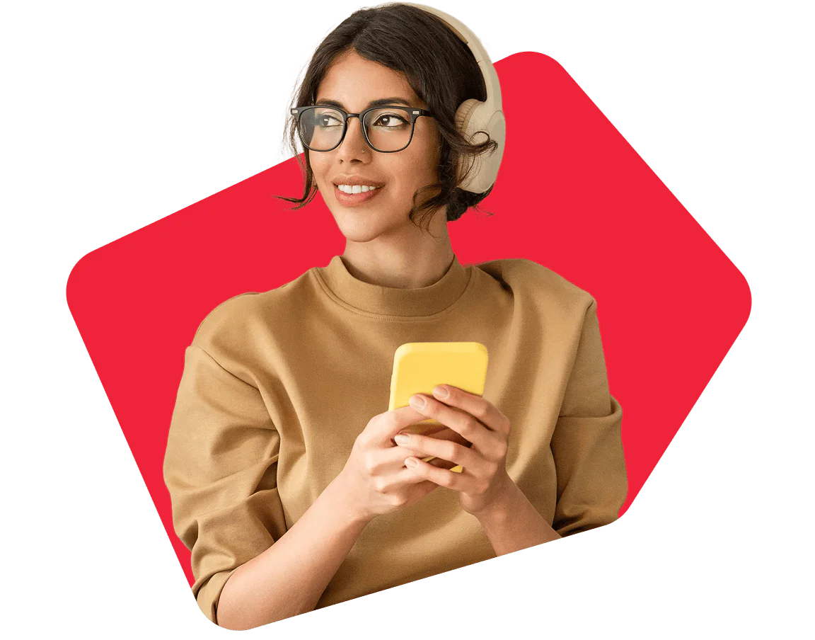 Woman with glasses wearing headphones holds a yellow smartphone against a red background.