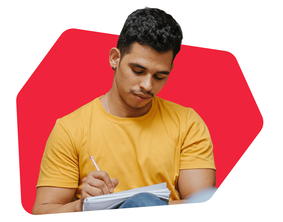Young man in yellow shirt writing in a notebook with a pen, red background