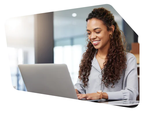 Smiling woman with curly hair typing on a laptop in a bright, modern office setting.