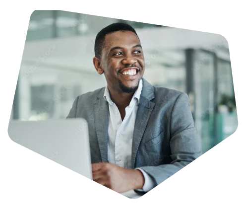 Man in grey suit smiling while working on his laptop in a modern office.