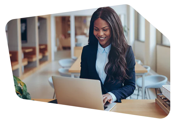 Woman in a suit smiling while working on a laptop in a modern office setting