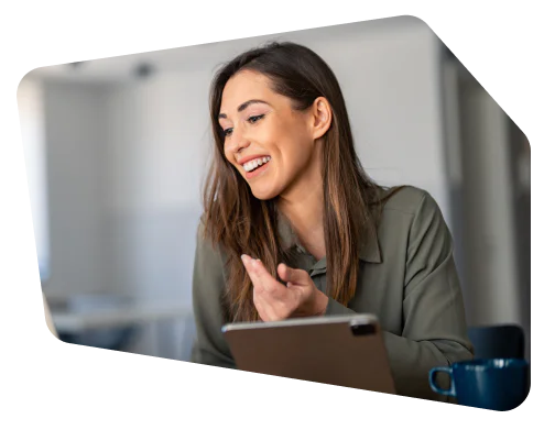 Smiling woman gesturing during a virtual meeting with a tablet and a coffee cup nearby.
