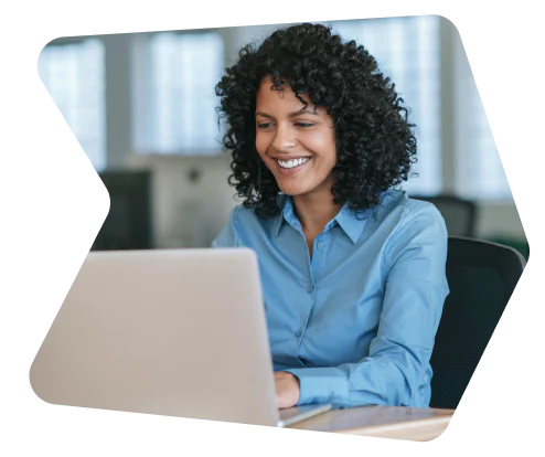 Woman with curly hair smiling while using a laptop in an office setting.