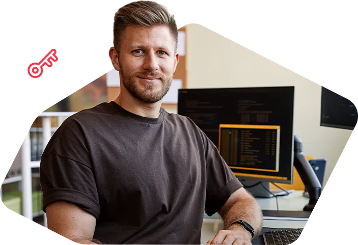 Man sitting at a desk with two monitors in an office, smiling at the camera.