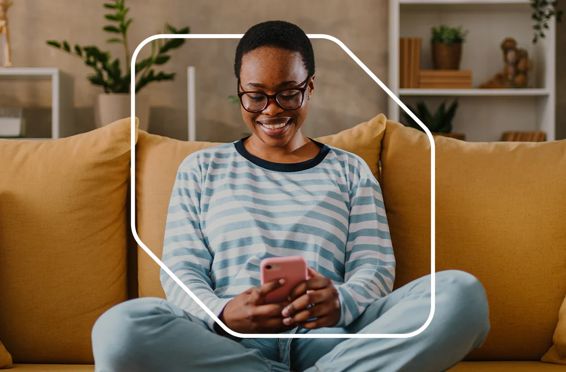 Smiling person sitting on a yellow couch using a smartphone.