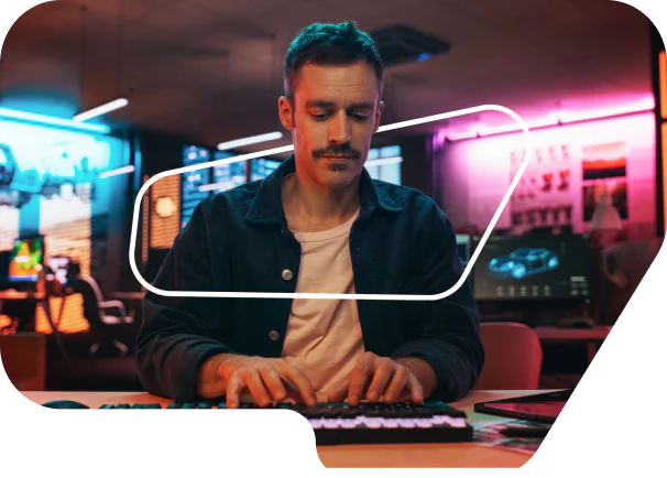 Man concentrating on typing at a computer in a vibrant, neon-lit office space.