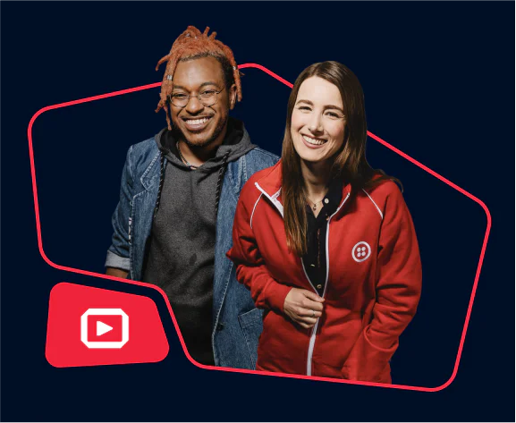 Two people smiling, one wearing a denim jacket and the other in a red hoodie with a logo.
