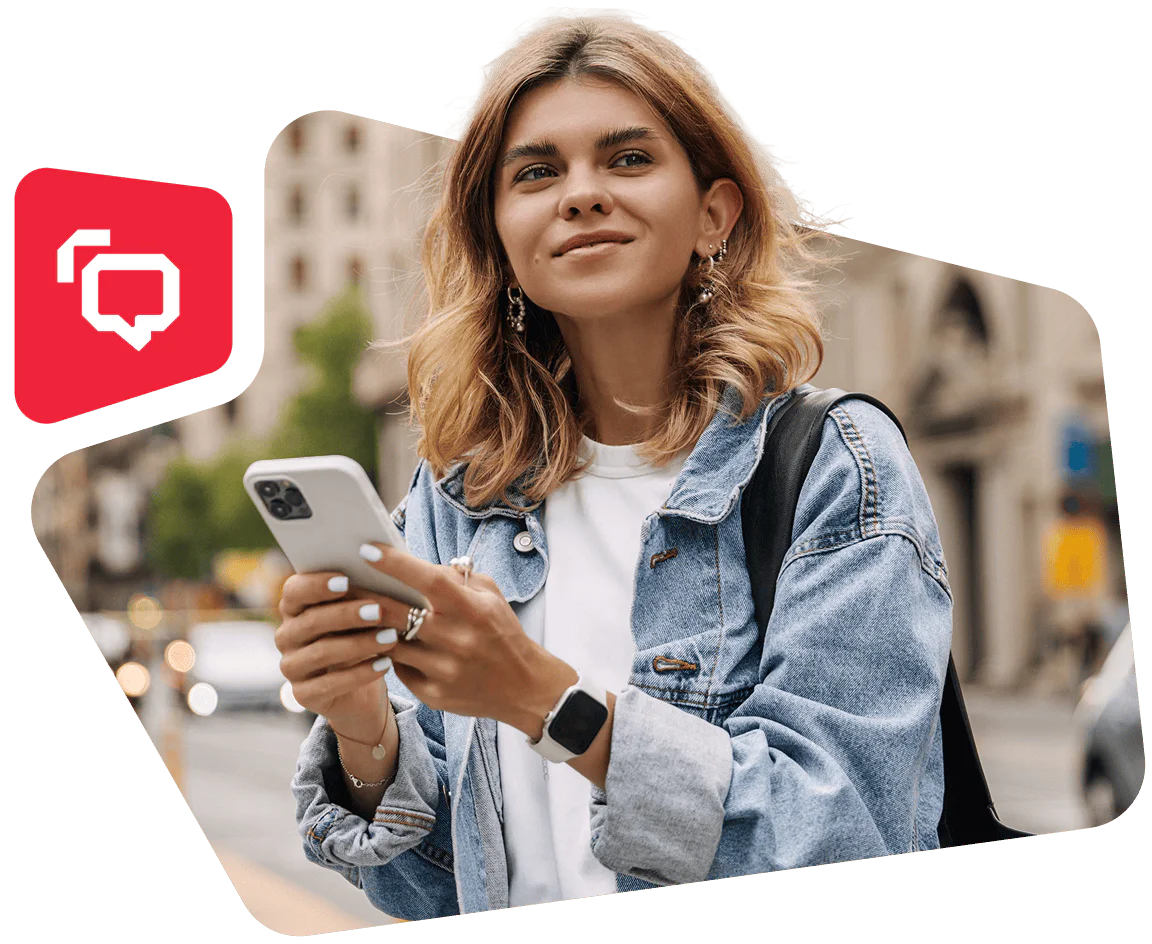 Woman in denim jacket holding a smartphone and smiling outdoors.
