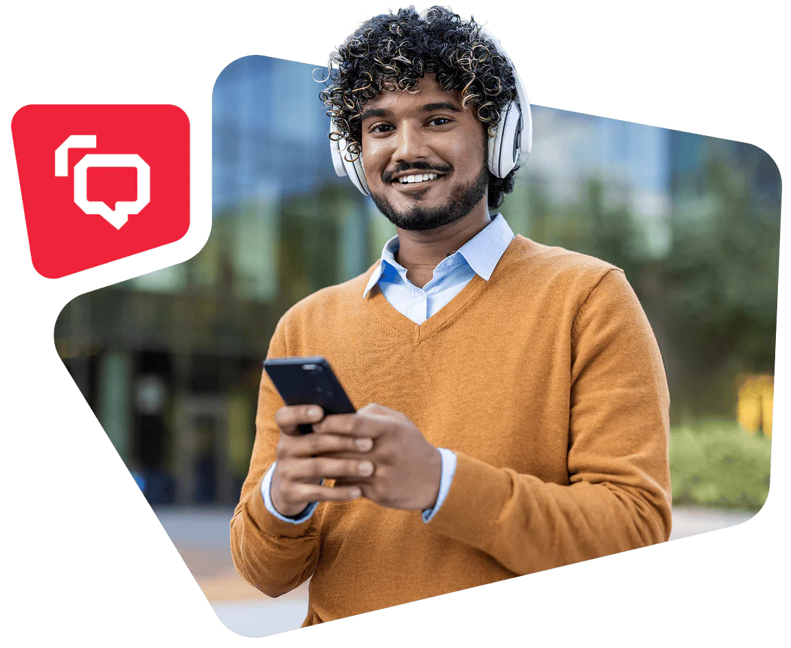 Man with curly hair, headphones, and orange sweater smiling while using a smartphone outside